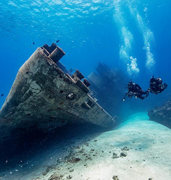 Two scuba divers in open water looking at a ship wreck.